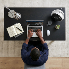 Person using a laptop at a desk with a notebook, pen, and other items.