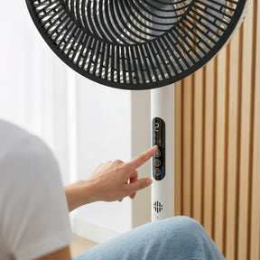 Person adjusting a standing fan with a control panel in a room.