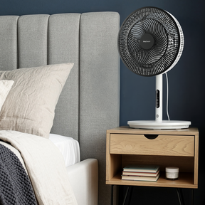 Table fan on a nightstand next to a bed with gray headboard and pillows.